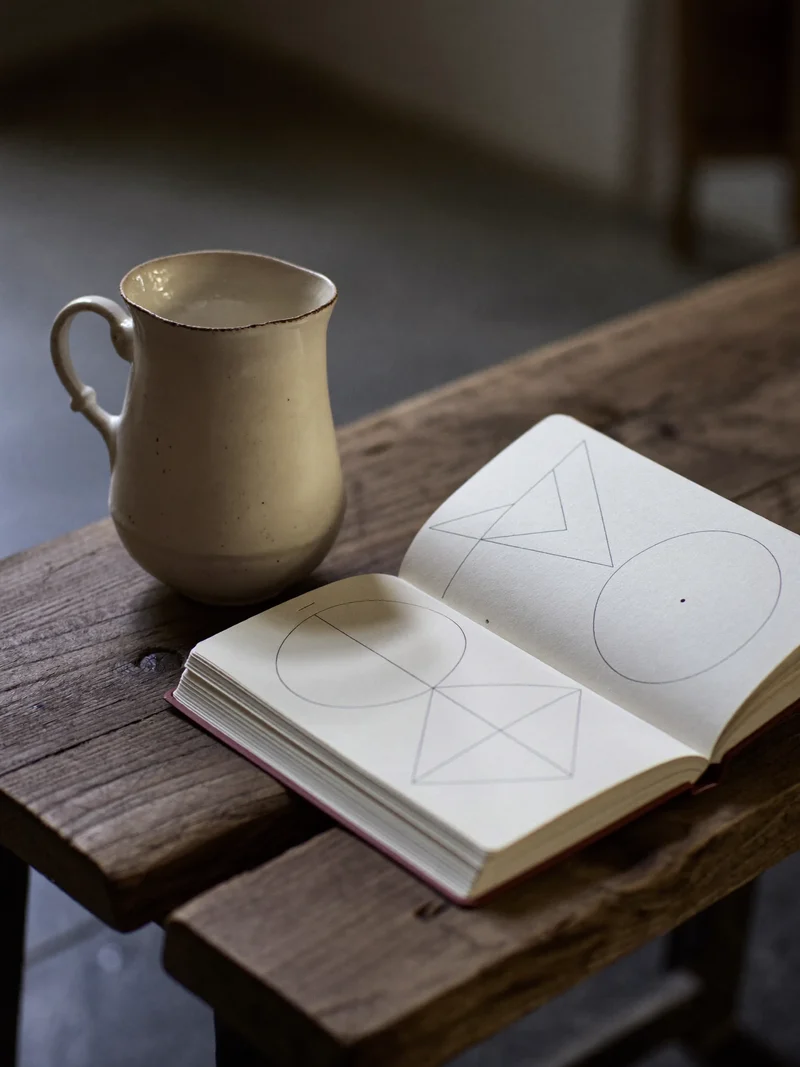 Åben notesbog med håndtegnede geometriske figurer ved siden af en keramikkop